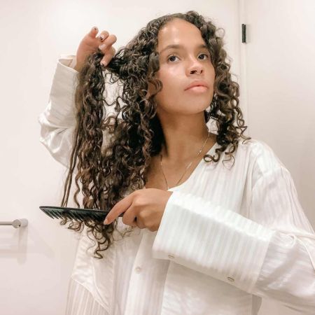 How to prevent static hair — woman with curly hair combing in white pajamas using Sillo silk pillowcase routine.