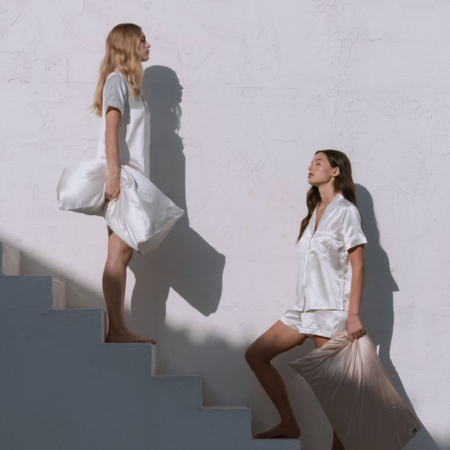 Two women in silk sleepwear holding Sillo silk pillowcases, symbolizing gentle, hypoallergenic care for acne-prone and sensitive skin.