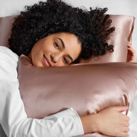 Woman with curly hair resting on a blush pink Sillo silk pillowcase made from 22-Momme mulberry silk that reduces frizz, prevents breakage, and keeps curls smooth, hydrated, and tangle-free overnight.