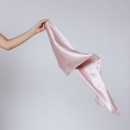 Hand holding a blush pink Sillo silk pillowcase made from 22-Momme mulberry silk — dermatologist-recommended for acne-prone and sensitive skin, infused with silver ions to reduce bacteria and promote clearer, healthier skin overnight.