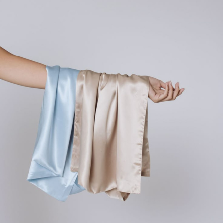 Light champagne and haze blue Sillo silk pillowcases draped over a hand — demonstrating gentle care and washing techniques for delicate silk fabrics.