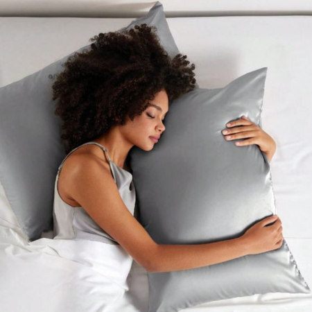 Discover how 22-Momme mulberry silk reduces frizz, breakage, and dryness for smoother, healthier strands. Image shows a woman sleeping peacefully on a silver Sillo silk pillowcase, highlighting its smooth texture and shine