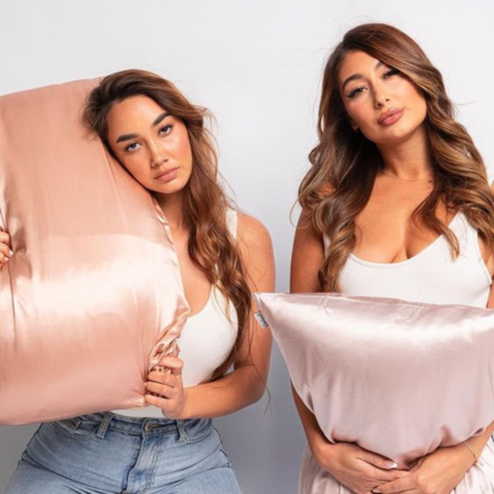 Two women holding blush pink Sillo silk pillowcases, highlighting the difference between silk and cotton for smoother skin, frizz-free hair, and temperature-regulated sleep.