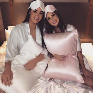Two women relaxing with Sillo silk pillowcases in blush pink and ivory — crafted from 22-Momme mulberry silk that reduces friction, prevents breakouts, and keeps hair smooth and skin hydrated overnight.