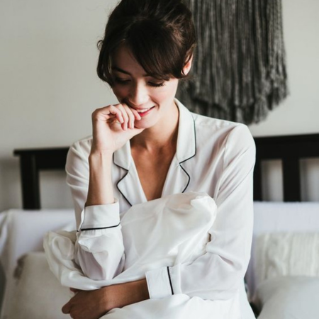 Woman in silk pajamas holding a white silk pillow, representing Sillo’s antimicrobial silk pillowcase designed to reduce bacteria and support clear, healthy skin.