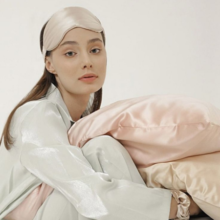 Woman in soft loungewear holding champagne and blush Sillo silk pillowcases, highlighting proper silk care and washing tips.