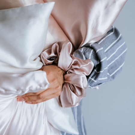 Comparing silk to satin — what’s the difference? Explore how Sillo silk pillowcases outperform satin. Image shows a close-up of hands holding blush and ivory Sillo silk pillowcases with a matching silk scrunchie