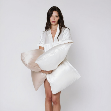 Woman in white sleepwear holding champagne and cream Sillo silk pillowcases — the ultimate travel essential for skincare and hair.