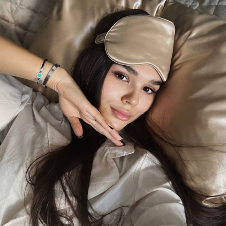 Woman resting on a champagne Sillo silk pillowcase, wearing a matching sleep mask — showcasing the connection between quality sleep, skin repair, and the benefits of silk for clearer, healthier skin.
