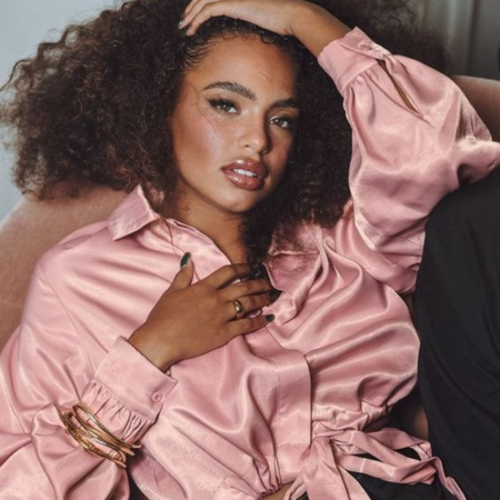 Woman with curly hair wearing a pink silk blouse — illustrating dry hair care and how Sillo silk pillowcases reduce breakage, friction, and split ends.