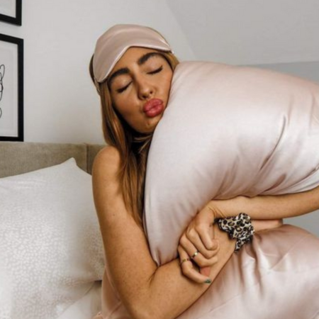 How Sillo silk pillowcases transform skin health and banish breakouts.Image shows a woman hugging a blush-pink Sillo silk pillowcase while wearing a matching silk sleep mask, symbolizing clear skin and restful beauty sleep.