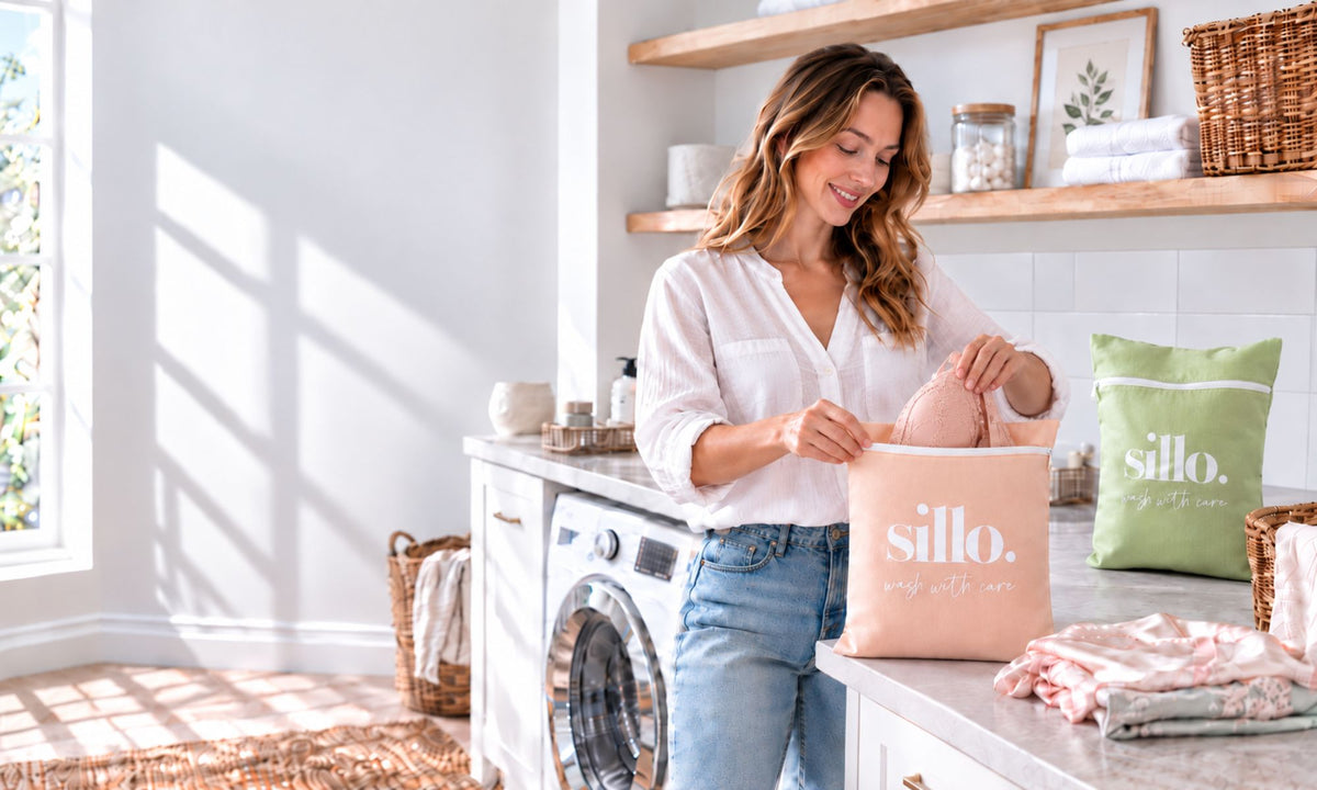 A woman in a bright laundry room smiles while placing her bras inside a Sillo care delicate laundry washbag that helps prevent tangles and maintain bras shape