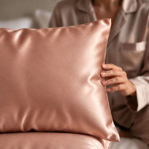 A close-up of a person in matching beige pajamas holding Rose Pink Sillo silk 22 momme mulberry silk pillowcase with envelope closure  in a softly lit bedroom setting.