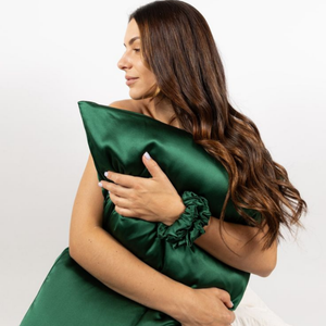 Lifestyle photo of woman holding Emerald Green Sillo silk pillowcase — soft 22-Momme organic Mulberry silk woven with silver ions for acne-prone, sensitive skin and hair; helps reduce wrinkles and signs of aging. Cooling, hypoallergenic, and gentle for daily use.