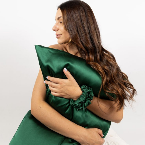 Lifestyle photo of woman holding Emerald Green Sillo silk pillowcase — soft 22-Momme organic Mulberry silk woven with silver ions for acne-prone, sensitive skin and hair; helps reduce wrinkles and signs of aging. Cooling, hypoallergenic, and gentle for daily use.