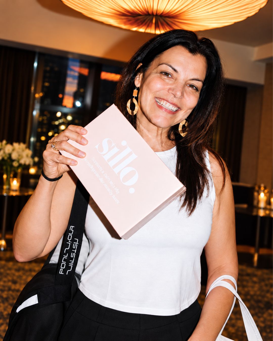Real Sillo customer smiling as she holds a Sillo silk pillowcase gift set, which includes two 22 momme 6A grade silk pillowcases woven with silver ions and care wash bag.  