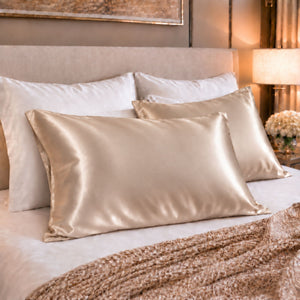 A set of Sillo light champagne 22 momme mulberry silk pillowcases woven with silver ions, arranged on a bed with a matching beige headboard and a textured knit throw blanket.