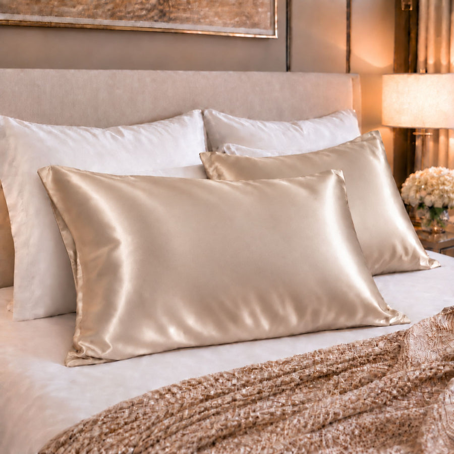 A set of Sillo light champagne 22 momme mulberry silk pillowcases woven with silver ions, arranged on a bed with a matching beige headboard and a textured knit throw blanket.