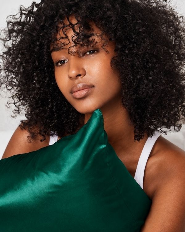 A women with curly hair holding a Sillo emerald green 22 momme mulberry silk pillowcase for curly hair helps prevent breakage frizz 