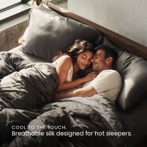 Charcoal Grey Sillo silk pillowcase styled on bed in modern bedroom; 22 Momme Mulberry silk woven with silver ions for acne-prone, sensitive skin and hot sleepers seeking cool, temperature-regulating, wrinkle-reducing sleep.