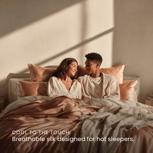 Rose Pink Sillo silk pillowcase styled on bed in modern bedroom; 22 Momme Mulberry silk woven with silver ions for acne-prone, sensitive skin and hot sleepers seeking cool, temperature-regulating, wrinkle-reducing sleep.