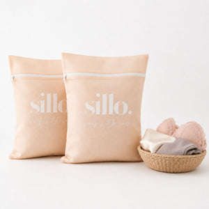 Sillo Care delicate laundry mesh washbags 2 pack in cream with zipper closure, standing upright beside a woven basket of lingerie and socks, mesh laundry bags for delicates protecting lingerie, bras, baby clothes, socks and activewear in the wash.