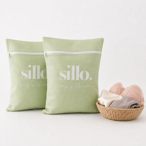 Sillo Care delicate laundry mesh washbags 2 pack in pistachio with zipper closure, standing upright beside a woven basket of lingerie and socks, mesh laundry bags for delicates protecting lingerie, bras, baby clothes, socks and activewear in the wash.