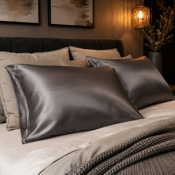Two charcoal grey Sillo silk pillowcases with envelope closure , 22 momme mulberry displayed on a neatly made bed in a warm, modern bedroom setting.