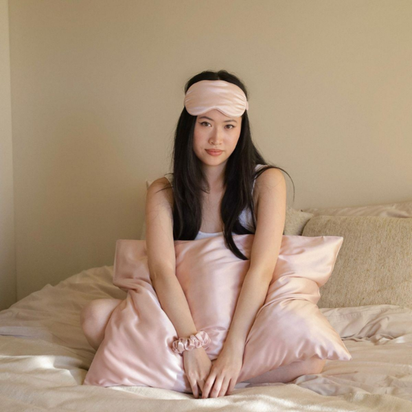 Blush Pink Sillo silk pillowcase styled on bed in modern bedroom; 22 Momme Mulberry silk woven with silver ions for acne-prone, sensitive skin and hot sleepers seeking cool, temperature-regulating, wrinkle-reducing sleep.