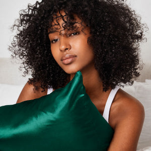 Lifestyle photo of woman holding Emerald Green Sillo silk pillowcase — soft 22-Momme organic Mulberry silk woven with silver ions for acne-prone, sensitive skin and hair; helps reduce wrinkles and signs of aging. Cooling, hypoallergenic, and gentle for daily use.