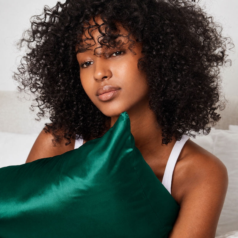 Lifestyle photo of woman holding Emerald Green Sillo silk pillowcase — soft 22-Momme organic Mulberry silk woven with silver ions for acne-prone, sensitive skin and hair; helps reduce wrinkles and signs of aging. Cooling, hypoallergenic, and gentle for daily use.